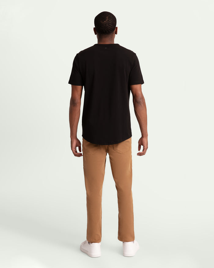 Man wearing black short-sleeve t-shirt and tobacco brown slim fit pants with white socks, shown from behind.