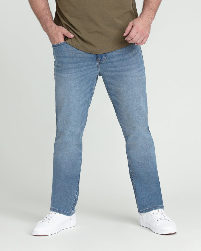 Man wearing light indigo straight-leg jeans with olive t-shirt and white sneakers.