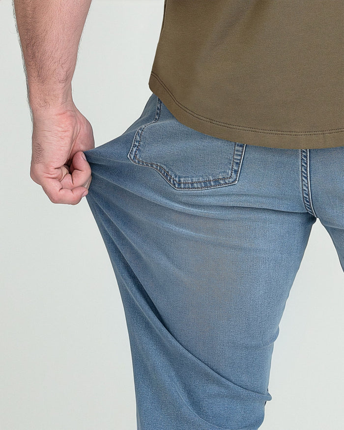 Light indigo jeans with curved back pockets and stitching detail, shown on model wearing olive shirt.