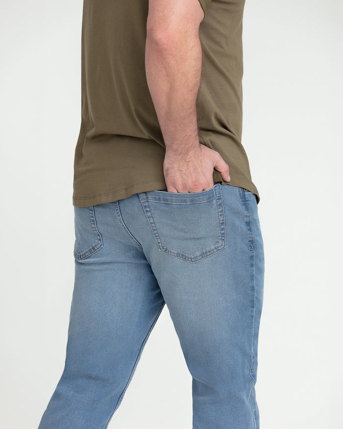 Light indigo slim fit jeans with five-pocket styling worn with olive t-shirt.