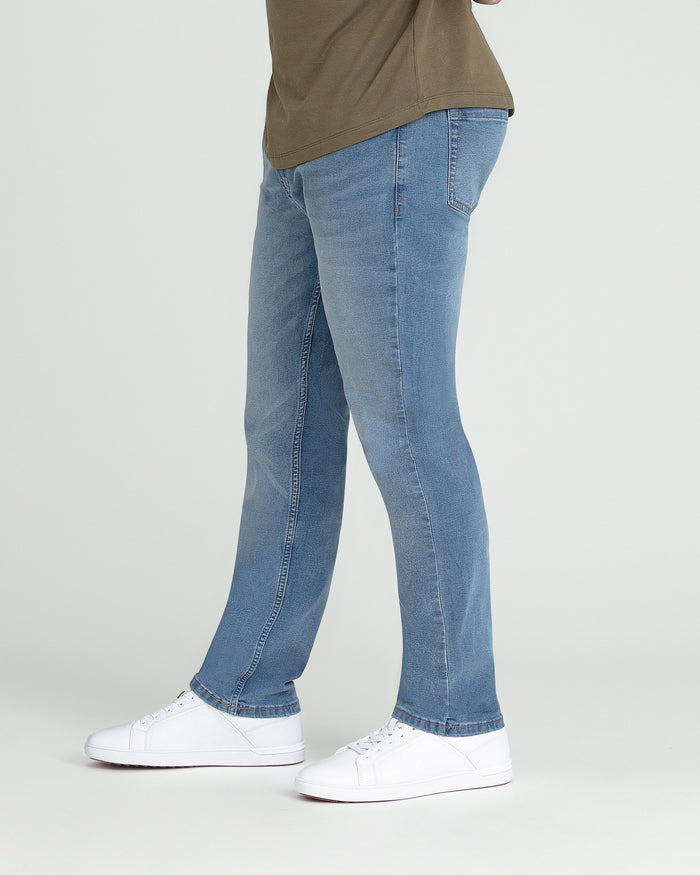 Light indigo jeans with a straight leg fit, shown with a tan shirt and white sneakers.