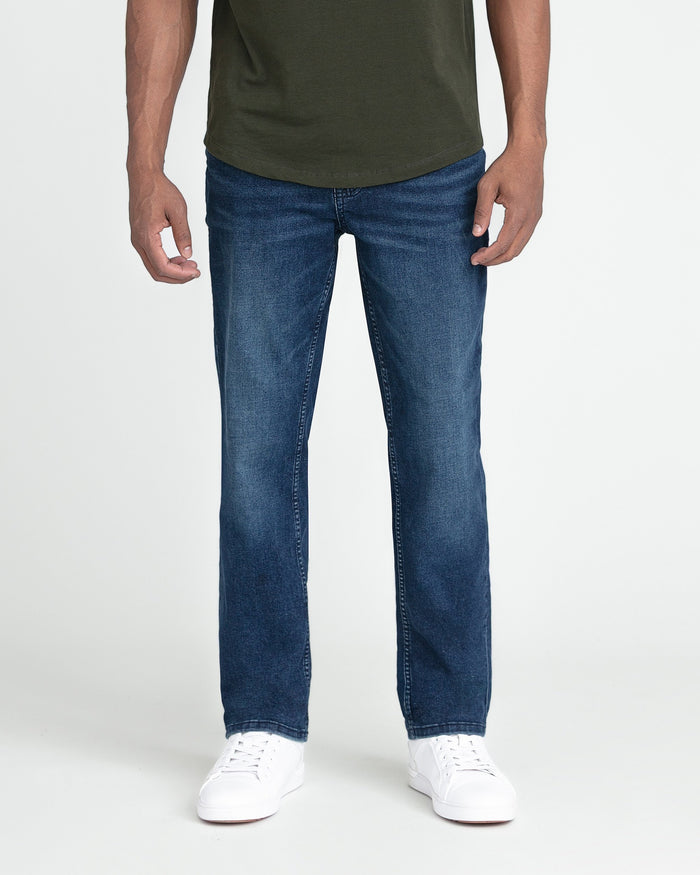 Man wearing dark blue slim fit jeans with olive green t-shirt and white sneakers.