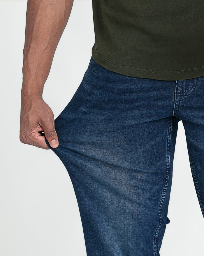 Man wearing olive green t-shirt and dark blue jeans, showing fit around torso and thigh area.