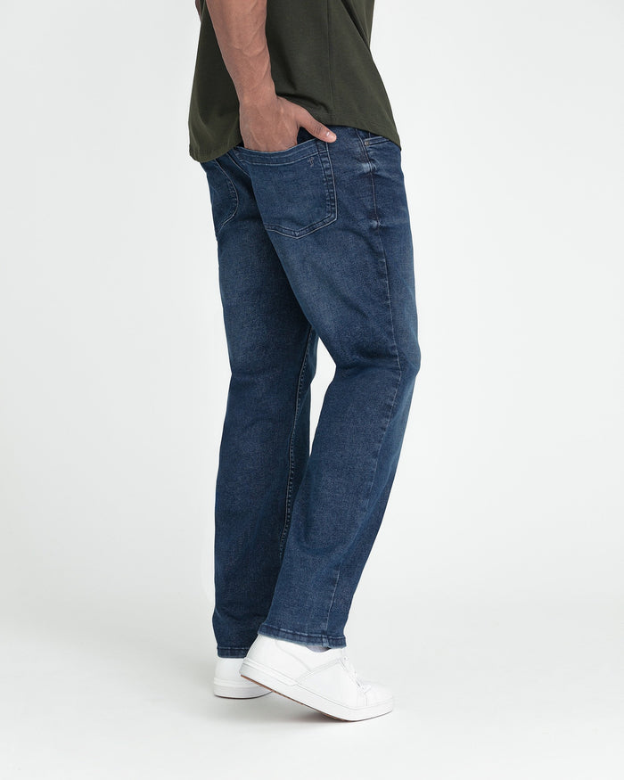 Man wearing dark blue jeans with straight leg fit and white sneakers, paired with olive green shirt.
