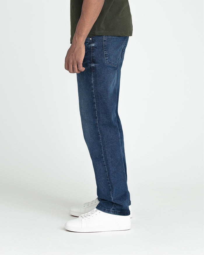 Dark blue slim fit jeans with straight leg, shown on model wearing white sneakers.