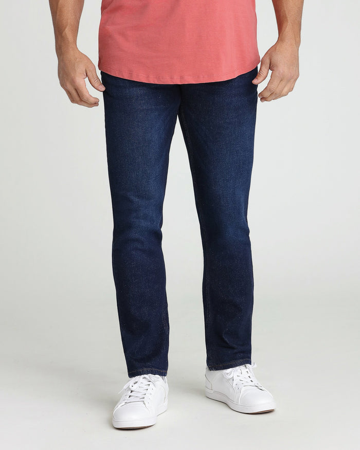 Man wearing dark blue slim fit jeans with coral pink t-shirt and white sneakers.