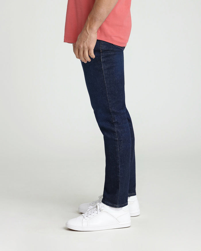 Man wearing dark blue slim fit jeans with pink shirt and white sneakers, shown from side view.
