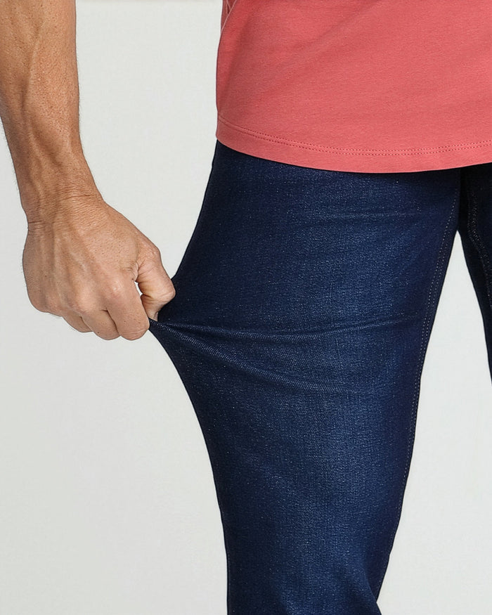 Dark blue slim fit jeans with coral pink shirt worn by a man showing waistband detail.