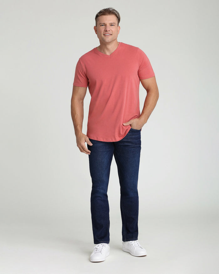 Man wearing coral v-neck t-shirt and dark blue slim fit jeans with white sneakers.