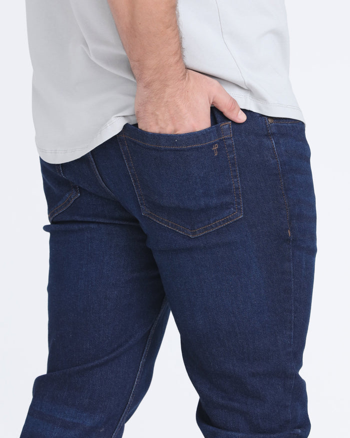 Dark blue denim jeans with visible rear pocket and contrast stitching, worn with white shirt.