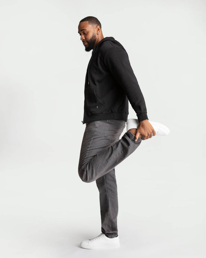 Man wearing black hoodie, grey denim jeans, and white sneakers, posed in profile.