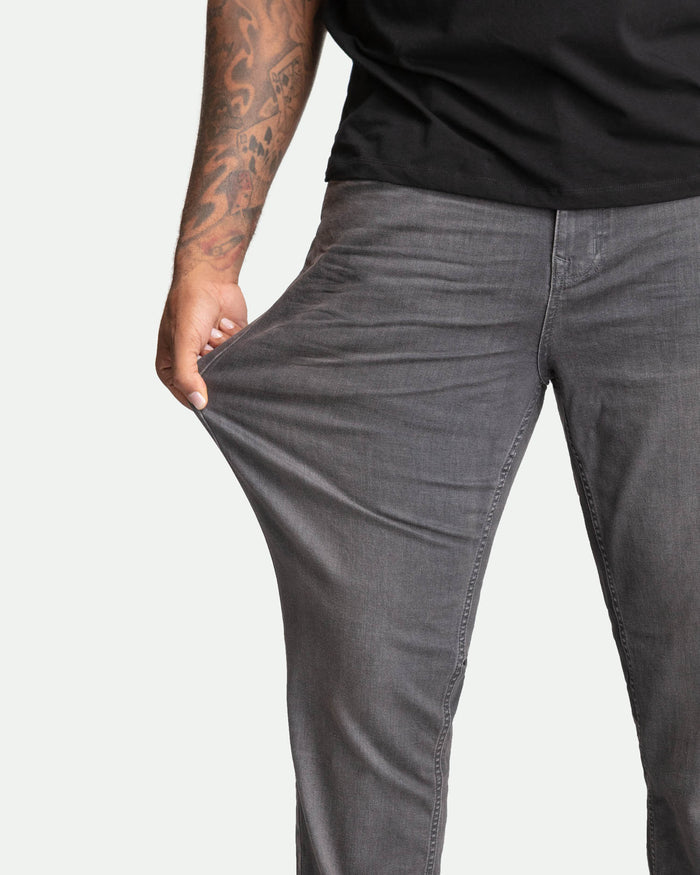Man wearing black t-shirt and grey slim-fit jeans with hand in front pocket.