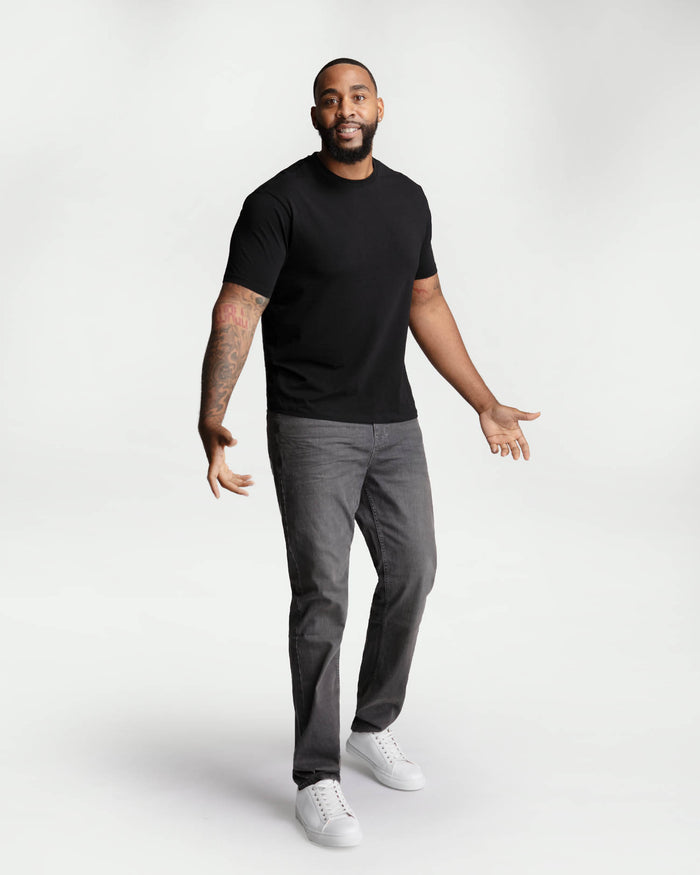 Man wearing black short-sleeve t-shirt and grey jeans with white sneakers.