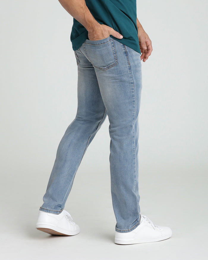 Man wearing light blue slim fit jeans with a teal shirt and white sneakers.