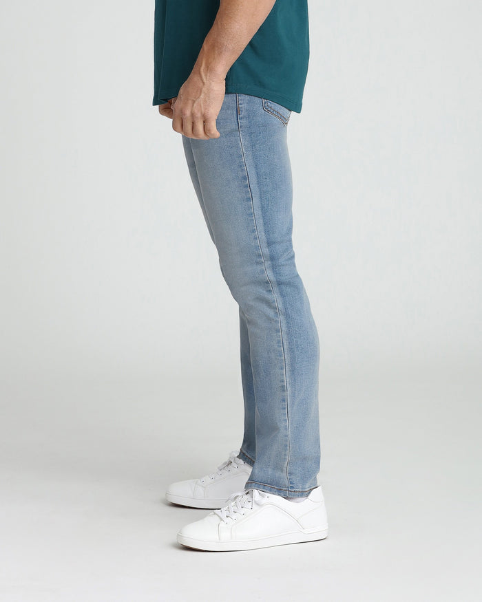Man wearing light blue slim fit jeans with dark teal t-shirt and white sneakers, side view.