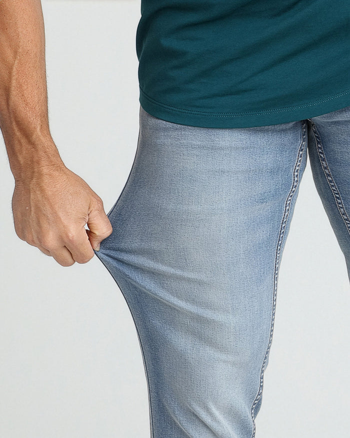 Man wearing dark teal t-shirt and light blue jeans, shown from waist down on right side.