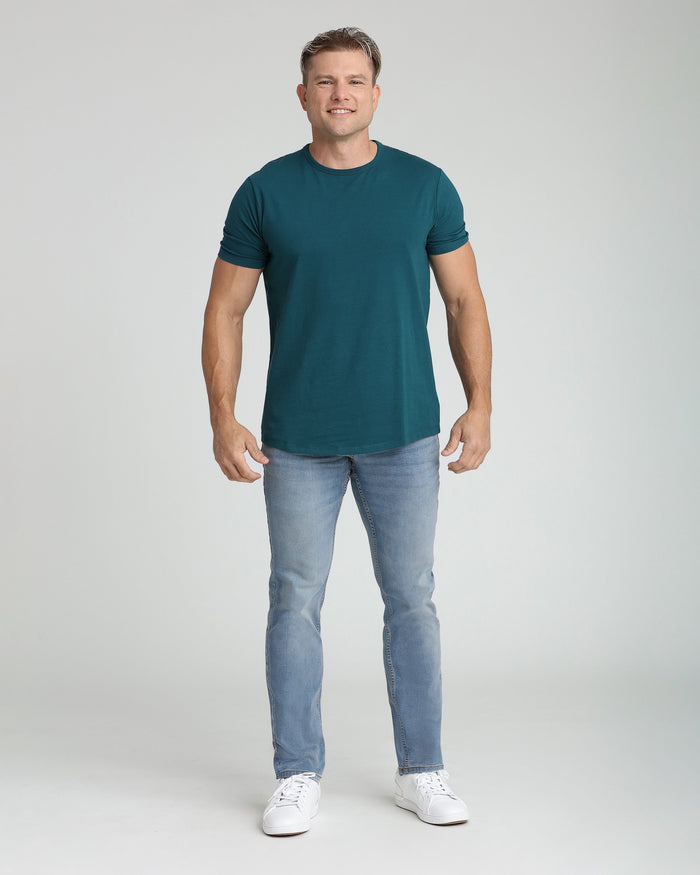 Man wearing dark teal short-sleeve crew neck t-shirt with light blue jeans and white sneakers.
