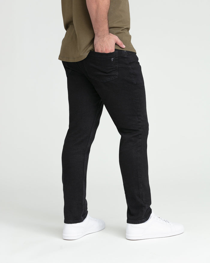 Black slim fit jeans with tapered leg on model wearing olive shirt and white sneakers.