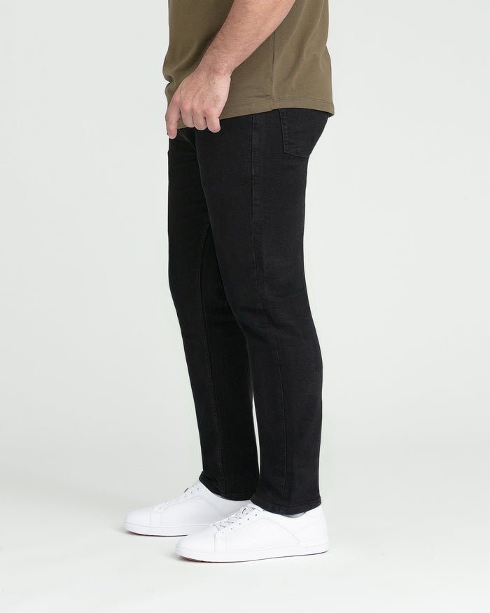Black slim-fit jeans worn with olive shirt and white sneakers, shown from the side.