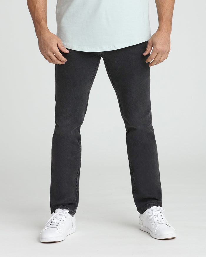 Faded black slim fit jeans on male model wearing white t-shirt and white sneakers.