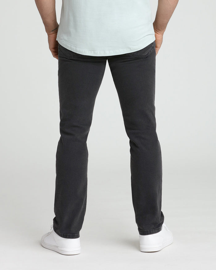 Faded black slim fit jeans shown from back on model wearing white t-shirt and white sneakers.
