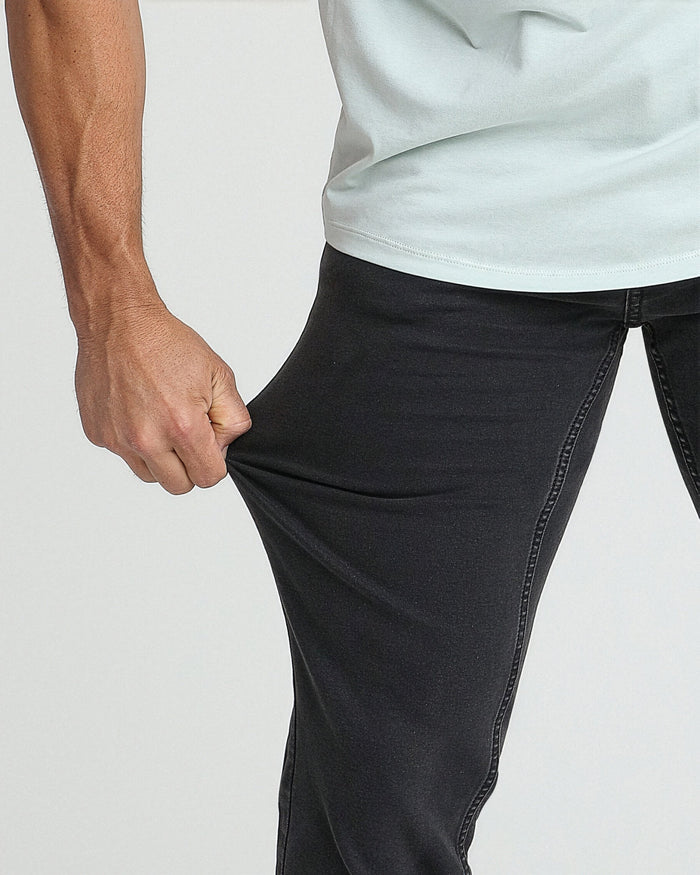 Man wearing faded black slim fit jeans with white t-shirt, showing thigh and waistband detail.
