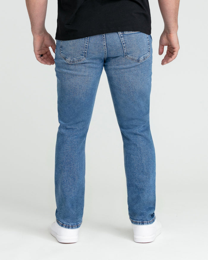 Man wearing medium blue slim fit jeans with black shirt and white sneakers, shown from behind.