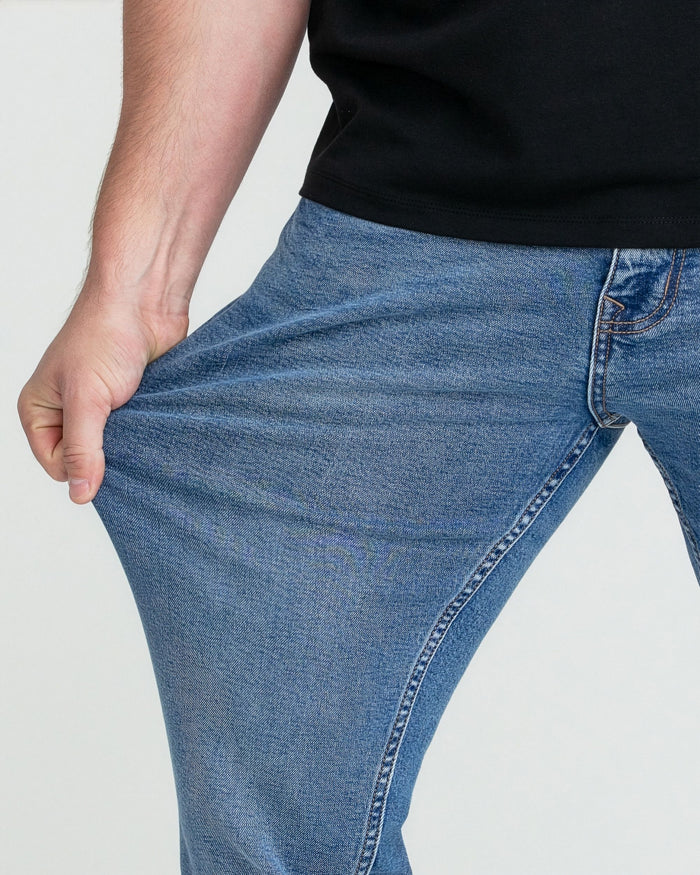 Man wearing medium blue slim fit jeans with black shirt, demonstrating fabric stretch.