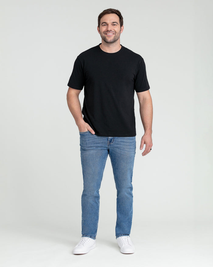 Man wearing black short-sleeve t-shirt and medium blue slim-fit jeans with white sneakers.