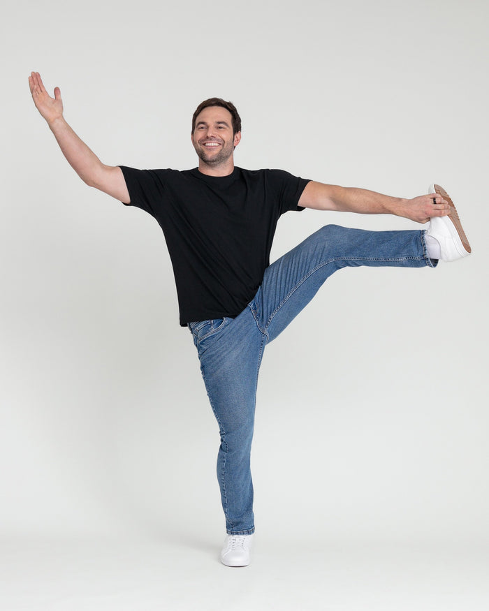 Man wearing black t-shirt and medium blue slim fit jeans with white socks and sneakers.