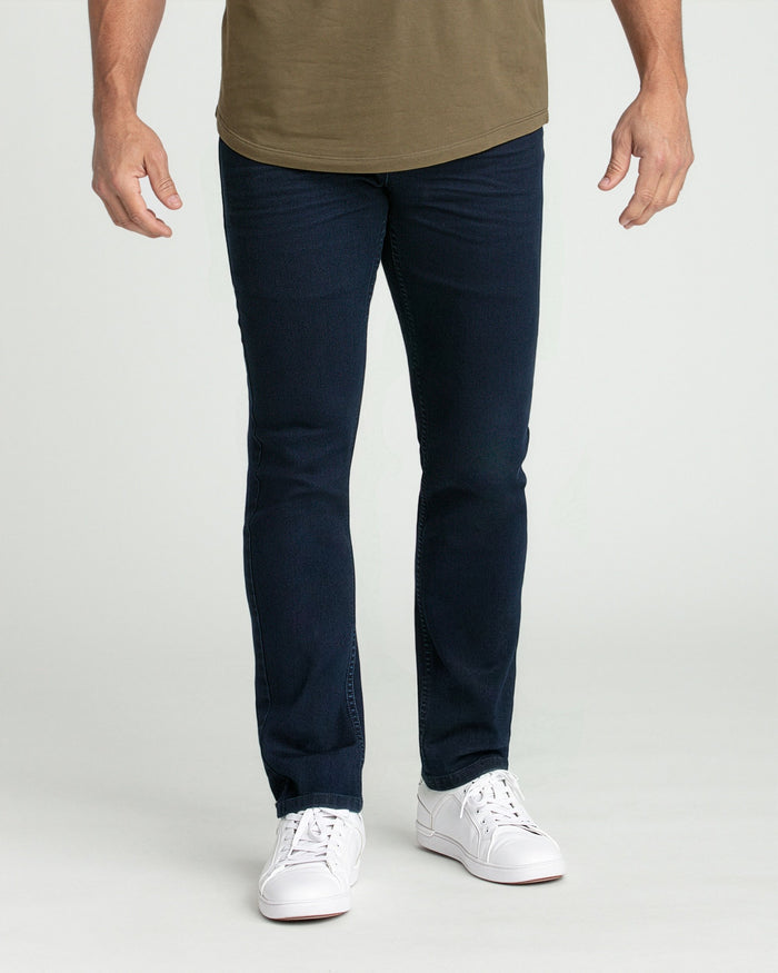 Man wearing deep blue slim fit jeans with olive t-shirt and white sneakers.