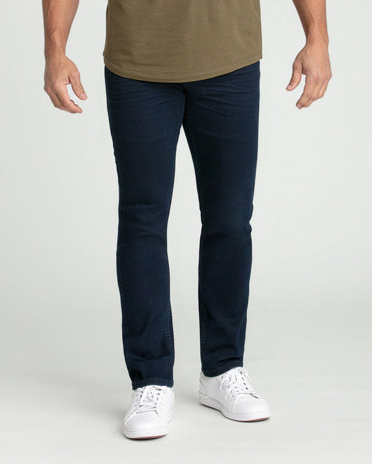 Man wearing deep blue slim fit jeans with olive t-shirt and white sneakers.