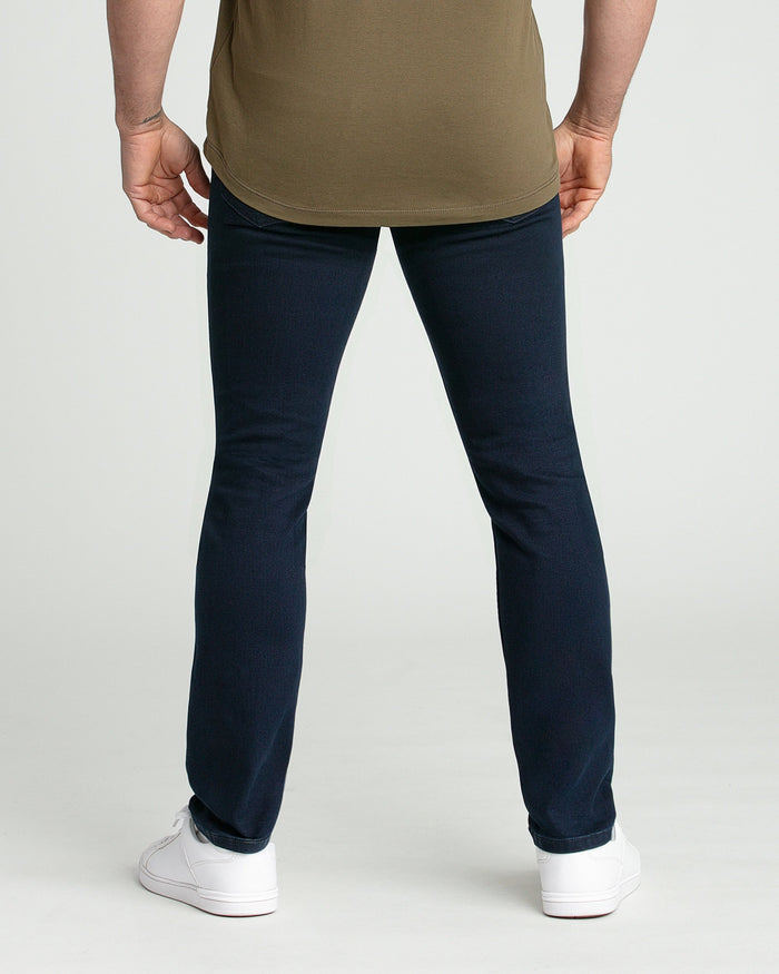 Man wearing olive-green t-shirt and dark blue slim-fit jeans with white sneakers, back view.