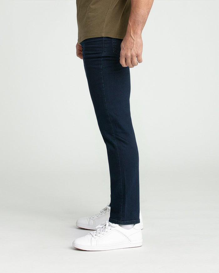 Man wearing deep blue slim fit jeans and white sneakers with olive short-sleeve shirt.