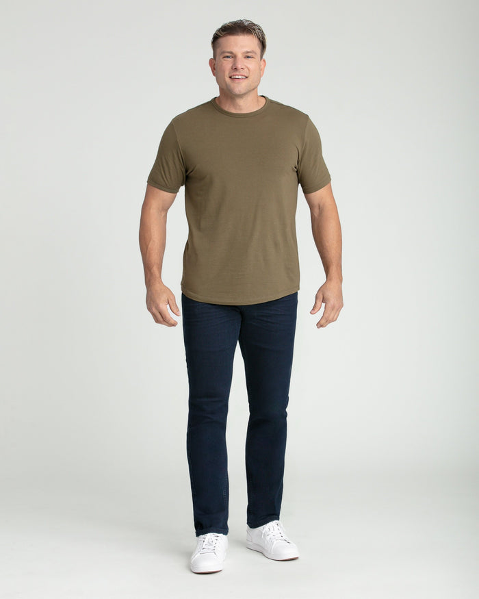 Man wearing olive green short-sleeve crewneck t-shirt with dark blue slim fit jeans and white sneakers.