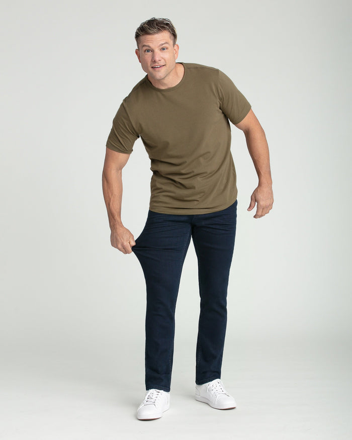 Man wearing olive-brown crew neck t-shirt with dark blue slim fit jeans and white sneakers.