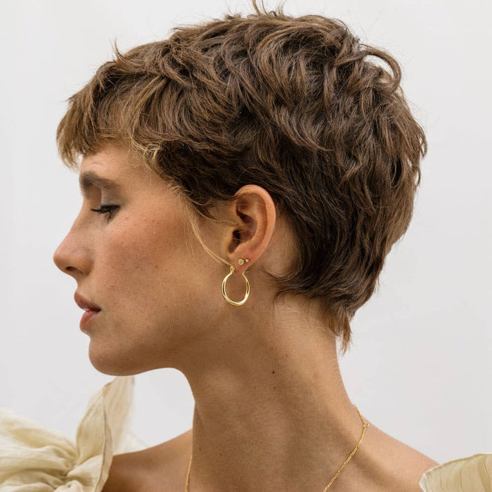 A person viewed from the side wearing small gold hoop earrings.
