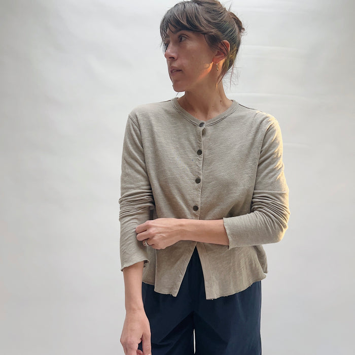Three-quarter front view of model wearing North Star Base artichoke snap-front cardigan open, showing crew neckline, snap placket, raw hem, and cropped length