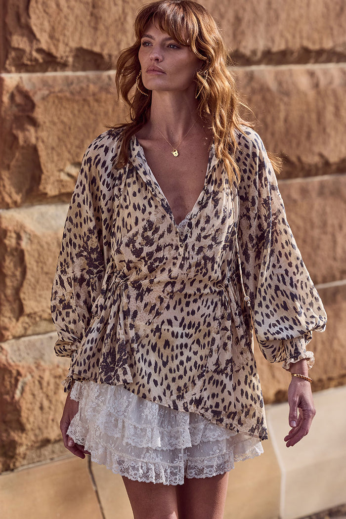 Front view of a model wearing Snow Leopard Asymmetric Blouse, showing front placket, neck ties and shirred cuffs