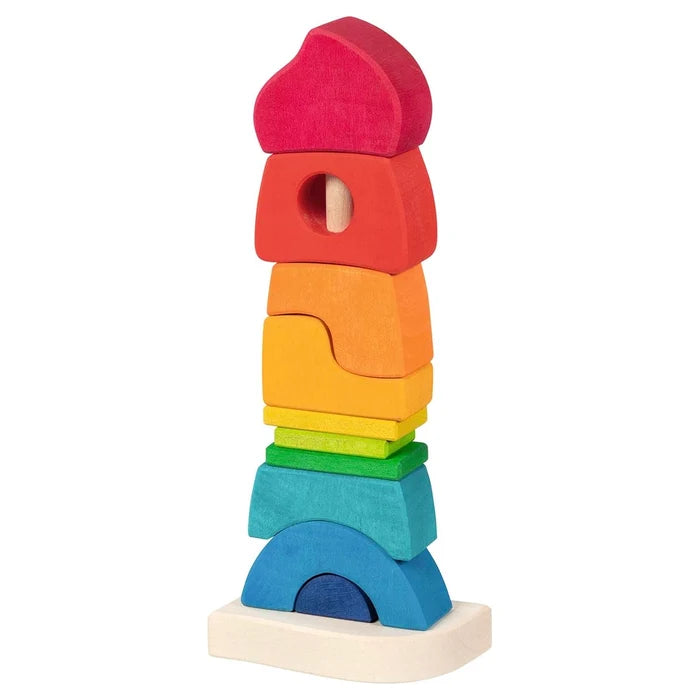 Goki Stacking Castle wooden toy fully assembled on a white background, showing rainbow-colored blocks stacked on a wooden rod from a wide blue arch base through green, yellow, orange, and red pieces up to a pink rounded top piece