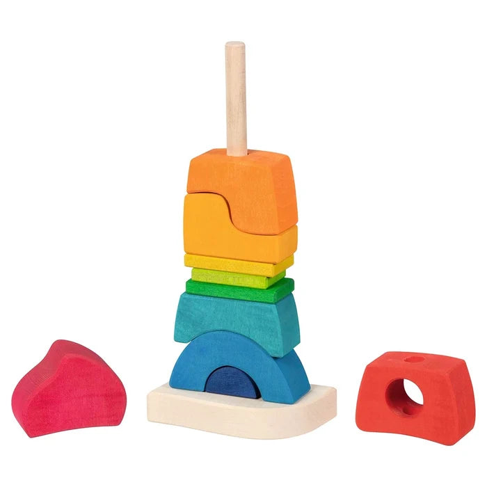 Goki Stacking Castle partially assembled on its wooden rod base, with the pink and red castle-top pieces removed and placed beside it, showing the full set of rainbow-colored wooden blocks including arches, rectangles, and irregular shapes