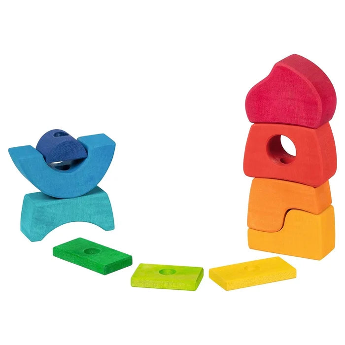 All pieces of the Goki Stacking Castle spread out and arranged in two free-standing groups on a white background, showing the full set of rainbow-colored wooden blocks including arches, flat rectangles, and irregular castle-shaped pieces in blue, teal, green, yellow, orange, red, and pink