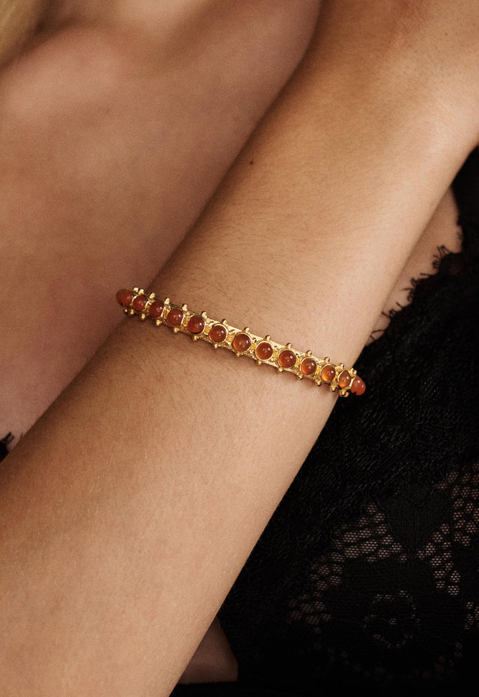 Close-up of gold brass cuff with carnelian stone settings worn on wrist, black lace top in background