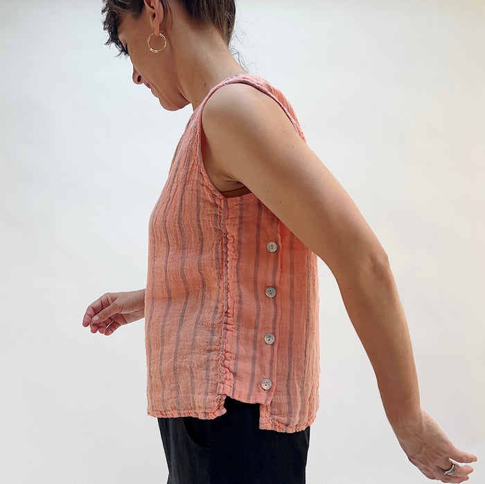Person wearing a pink sleeveless shirt with vertical stripes against a plain background, viewed from the side