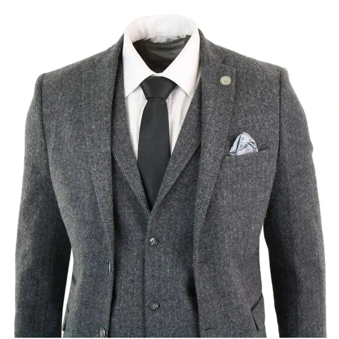 Men's grey and black herringbone tweed suit with tailored fit, includes blazer, waistcoat, and trousers, styled with white shirt and black tie.
