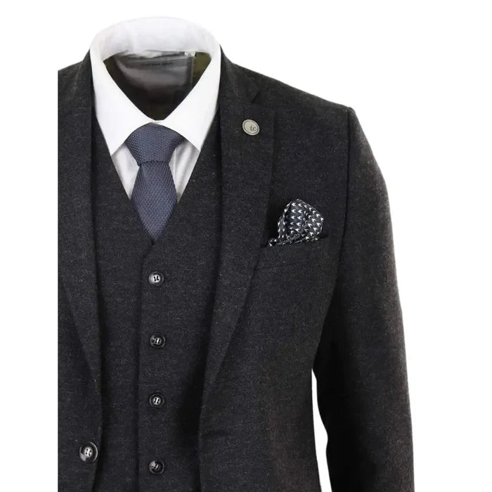 Dark gray men's wool tweed suit jacket with notch lapels, featuring a small metal lapel pin, and a pocket square with white dots, tailored fit.