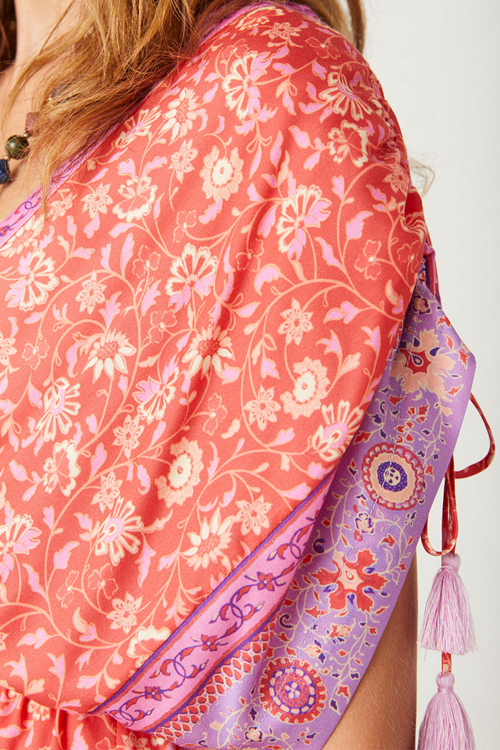 Close-up of coral floral print fabric with purple border print and adjustable shoulder tie with lilac tassel trim