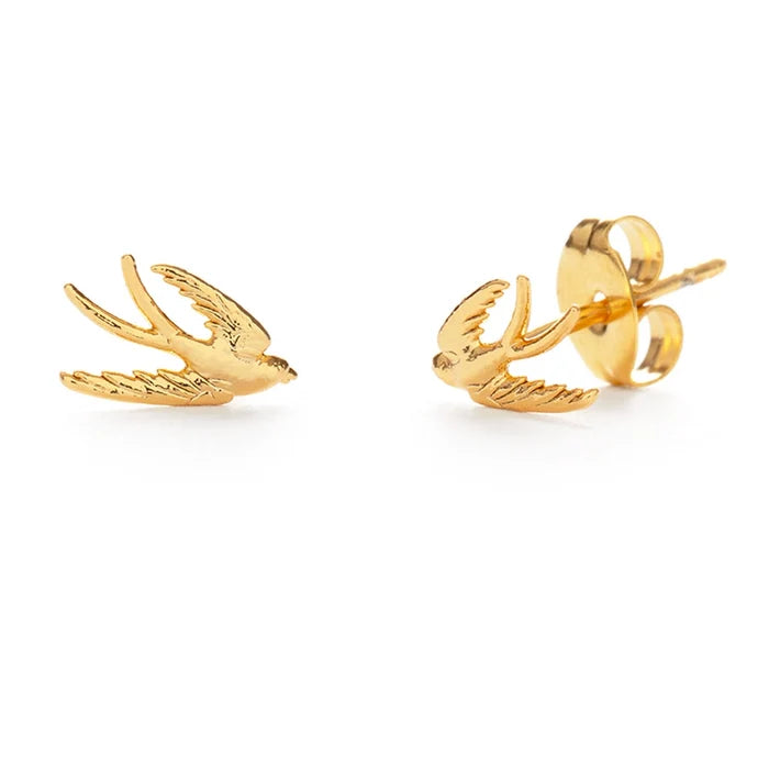 A pair of gold-colored swallow bird stud earrings against a white background.