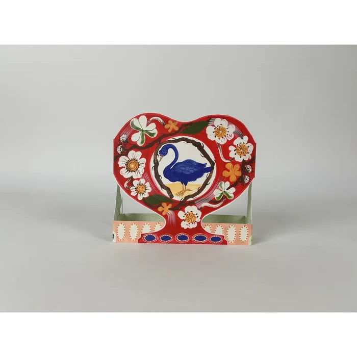 A pop-up card with a swan design on a red heart-shaped stand against a gray background
