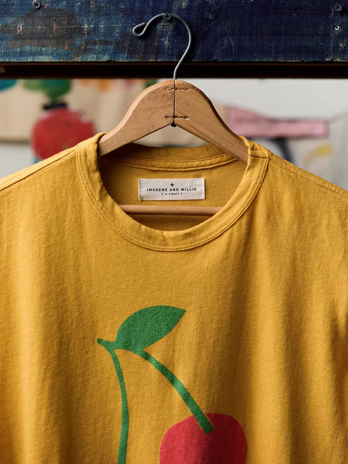 Close-up of the neckline of The Cherry Tee in Gold showing the Imogene and Willie label, ribbed crew neck, and the top of the cherry screen print with green stem and leaf on gold cotton